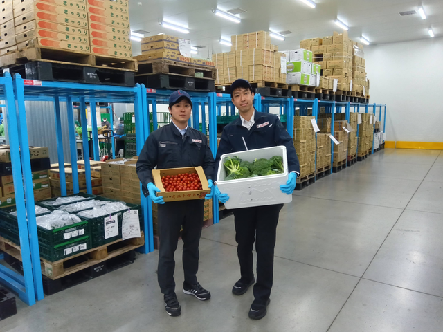 低温・生鮮の倉庫でトマトとブロッコリーを持って並ぶ２人