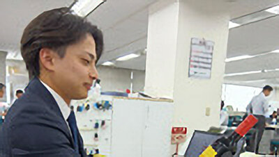 商品を見ながらデスクワークを行う男性社員の写真