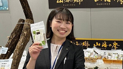 イベント会場で自社商品を手に笑顔で写る女性社員の写真