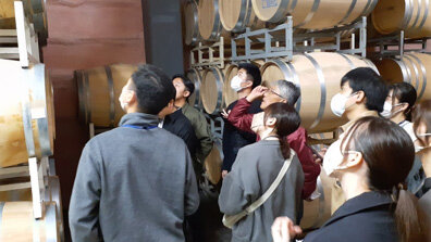 樽が並ぶ貯蔵庫を視察する社員の写真